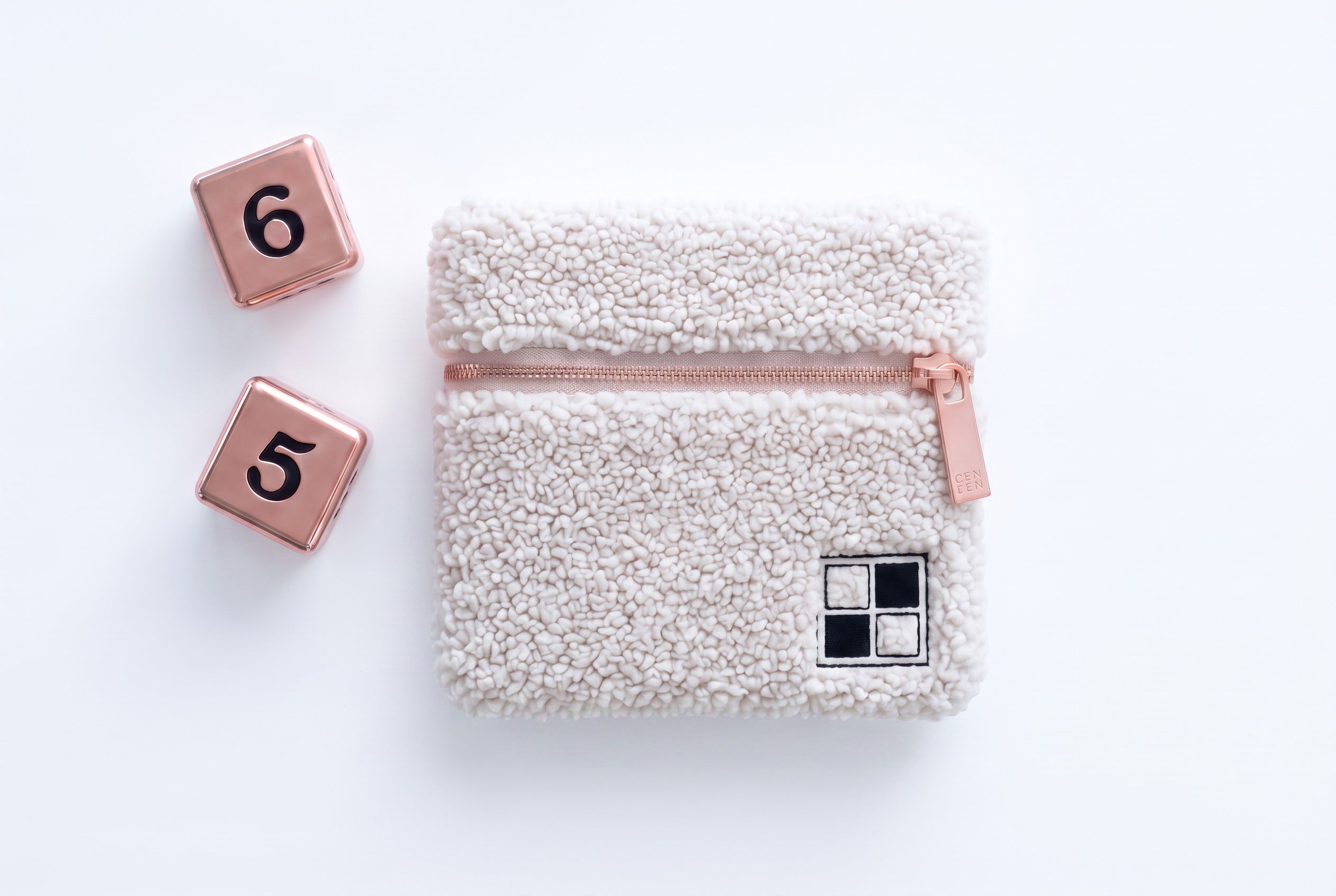 Two rose-gold dice beside the ivory bouclé storage pouch with embroidered Mise en Mahjong mark.