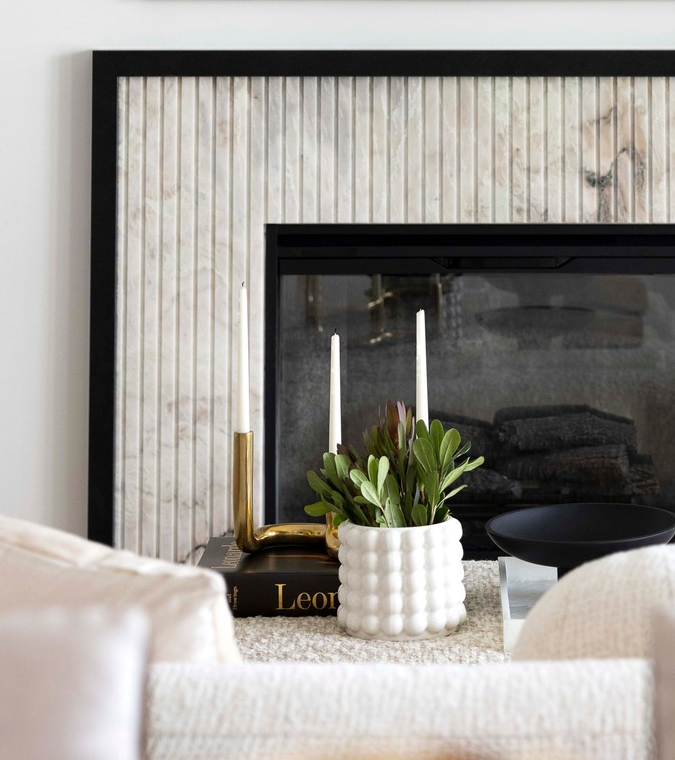 Fireplace vignette with white stone, brass candlesticks, potted plant and open book