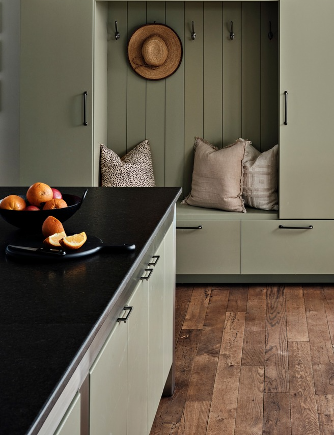 Sage green mudroom with vertical shiplap, brass hardware, fruit bowl on black counter