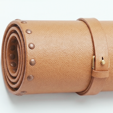 Rolled tan leather travel mat with brass stud trim and buckle closure